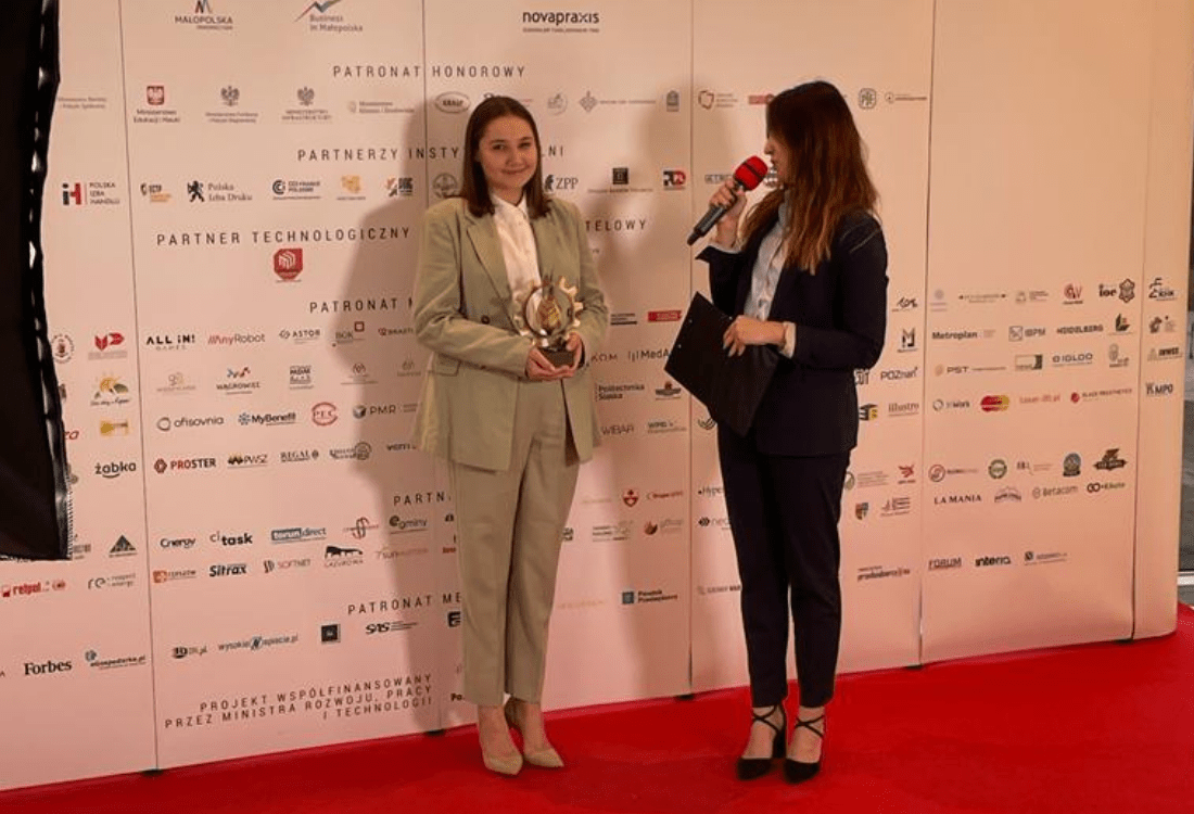 pracowniczka pst odbierająca złotą statuetkę ekostrateg obok stoi prowadząca galę z czerwonym mikrofonem