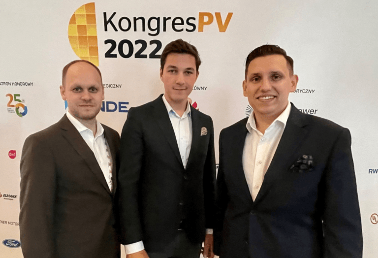 Trzech wiceprezesów Projekt Solartechnik na spotkaniu branży pv na ściance kongresu PV2022. Od lewej w brązowym garniturze Krzysztof Czajka wiceprezes do spraw sprzedaży. W środku w czarnym garniturze uśmiecha się Błażej Brasse wiceprezes do spraw technicznych. Po prawej stronie w czarnym garniturze Adam Goj wiceprezes do spraw handlowych.