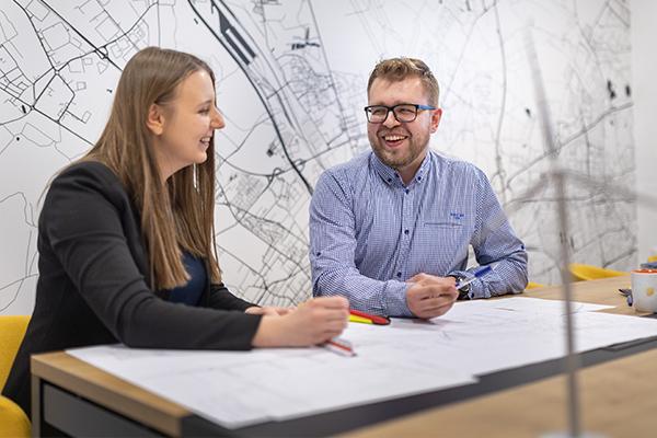 Dwoje uśmiechniętych pracowników Projekt Solartechnik siedzących w sali konferencyjnej nad danymi dotyczącymi rozwoju projektów fotowoltaicznych