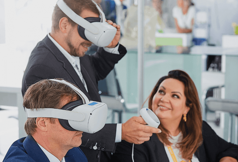 Na pierwszym planie dwóch mężczyzn w goglach rozszerzonej rzeczywistości w tle uśmiechnięta pracowniczka Projekt Solartechnik. Mężczyźni oglądają wizualizację farmy fotowoltaicznej w wirtualnej rzeczywistości.