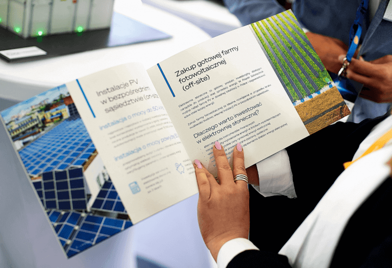 Na pierwszym planie trzymany w dłoniach ekspertki z Projekt Solartechnik Marty Rzepeckiej katalog firmowy w którym znaleźć można informacje na temat zakupu gotowej farmy fotowoltaicznej (off-site).